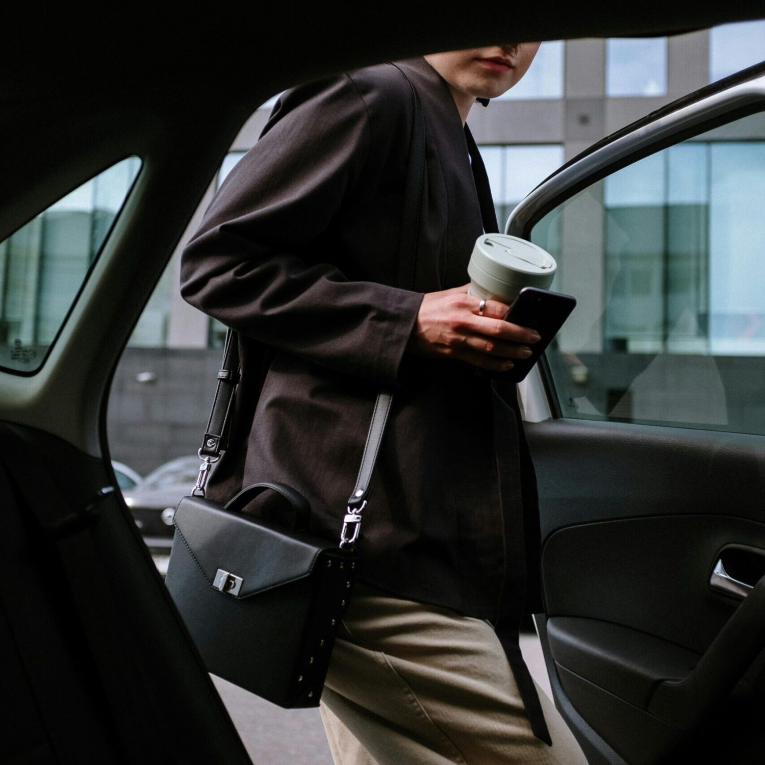 pexels-photo-4606397-4606397 Stylish woman entering a car, holding coffee and smartphone, showcasing urban lifestyle.